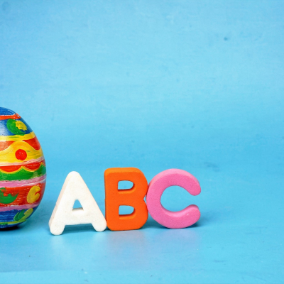 Ein bunt bemaltes Osterei steht neben den Schaumstoffbuchstaben A, B und C auf blauem Hintergrund.